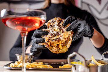 Woman in gloves holding juicy cheeseburger with cocktail