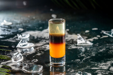 Layered cocktail shot with ice on dark surface