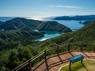 A heart-shaped inlet embraced by fresh green mountains, viewed from an observation deck. The calm emerald green sea and blue sky create a spectacular view conveying love and healing.