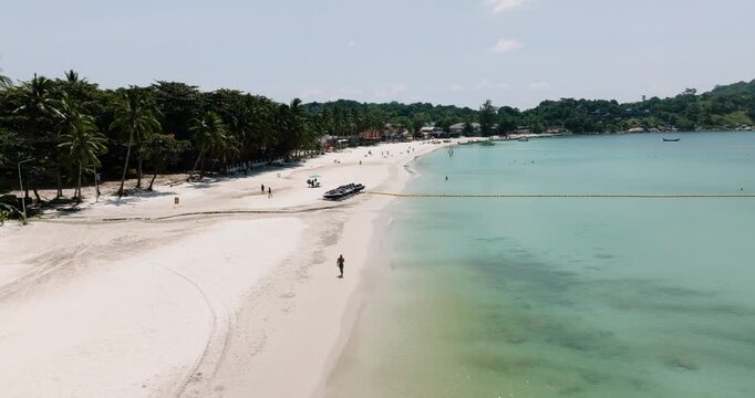 Sandy beach lined with palm trees and turquoise water on a sunny day. Haad Rin. Ko Pha Ngan, Thailand.