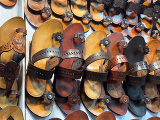 handcrafted leather sandals, likely Kolhapuri chappals, hanging for sale. The sandals are arranged in multiple rows and columns, showcasing a variety of designs and shades of brown leather.