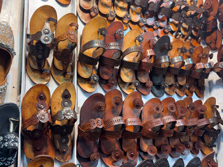 handcrafted leather sandals, likely Kolhapuri chappals, hanging for sale. The sandals are arranged in multiple rows and columns, showcasing a variety of designs and shades of brown leather.