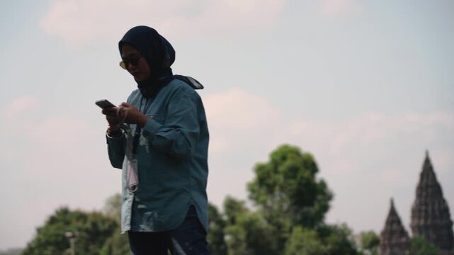 Asian muslim women solo traveler taking photos at Prambanan temple, Central java, Yogyakarta, Indonesia with his smartphone. Solo travel concept.