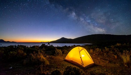 Illuminated tent under a starry night sky near a tranquil coastline