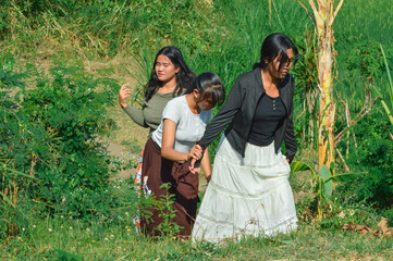 The girls walk together along a slightly elevated grassy path, surrounded by lush vegetation and...