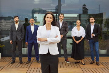 Smiling businesswoman stands on a rooftop terrace as colleagues and a diverse business team applaud...