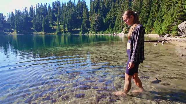 A young girl enjoys the clear, refreshing waters of Lake Valhalla, walking barefoot along its edge as part of her adventure on the Pacific Crest Trail in Washington