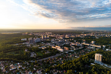 Aerial view of a city immersed in lush green forests at golden hour. Urban landscape with buildings, houses, and roads under a cloudy sky