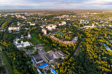 Aerial view of a green city with lush forests, modern residential buildings, and scattered urban infrastructure under a bright sky