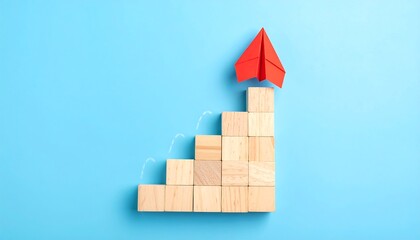 Wooden blocks form a staircase, red paper airplane on top, light blue background