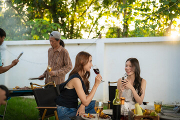 A group of multiracial friends are having a backyard dinner party, clinking beers or sharing drinks during happy hour. Young people are having fun together and clinking beers while standing in the gar