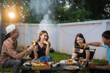 A group of multiracial friends are having a backyard dinner party, clinking beers or sharing drinks during happy hour. Young people are having fun together and clinking beers while standing in the gar