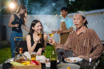 A group of multiracial friends are having a backyard dinner party, clinking beers or sharing drinks during happy hour. Young people are having fun together and clinking beers while standing in the gar