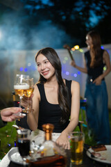 A group of multiracial friends are having a backyard dinner party, clinking beers or sharing drinks during happy hour. Young people are having fun together and clinking beers while standing in the gar