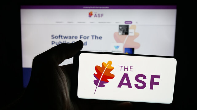 Stuttgart, Germany - 10-08-2025: Person holding mobile phone with logo of organisation Apache Software Foundation (ASF) on screen in front of web page. Focus on phone display.