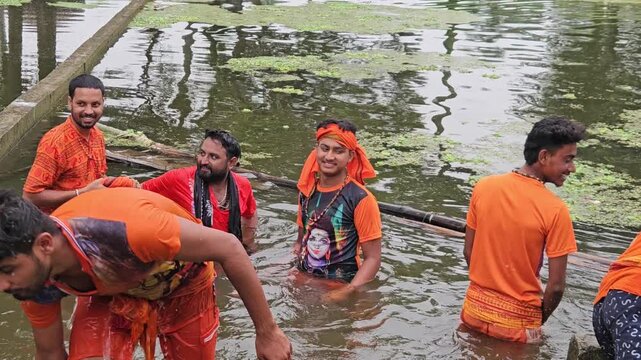 Kanwariya devotees dressed in saffron clothing collecting holy water from a village pond during the sacred Shravan Somwar Sawan Monday pilgrimage in India. The devotees prepare to carry the holy water