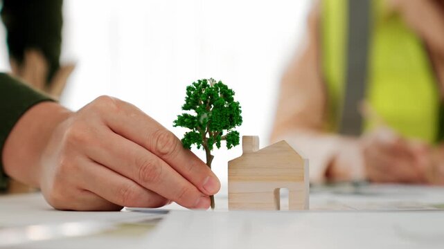 A video of architect using tree and home model to measure blueprint. Architect designing house construction on a table at studio, with architectural plan scattered around. Focus on hand. Delineation.