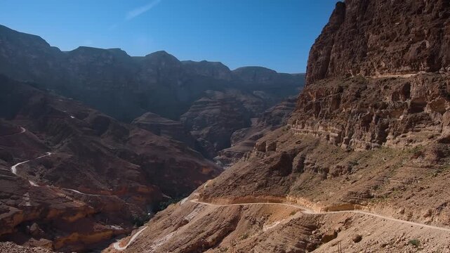 view of the rugged mountain terrain and a winding road leading to the village of Al Fahal in Oman. The footage captures the natural beauty of the Wadi Shab area, known for its dramatic canyons and sce