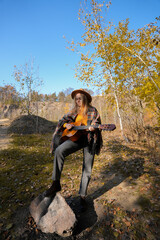 Portrait of smiling caucasian artist plays wooden acoustic guitar in autumnal park. Young songwriter plays string musical instrument hobby outside in nature fall time. Audio music healing in natural