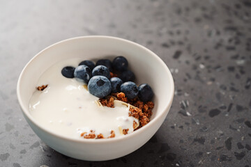 Healthy breakfast with whole grain granola and fresh blueberries in white bowl on concrete background