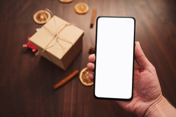 Man hand hold smarthone with white screen with christmas decorations on background