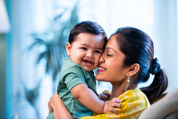 Young Indian mom holding her baby boy on sofa, expressing love and joy of motherhood