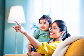 Young Indian mom holding her baby boy on sofa, expressing love and joy of motherhood
