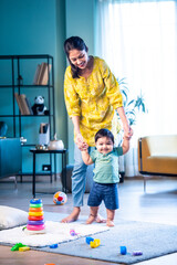 Indian Mother guiding infant boy to walk, holding hands in bright modern living room at home