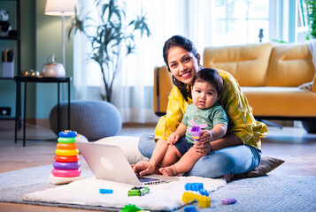 Young Indian mother working at home with infant son on lap, balancing life and care