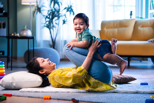 Fototapeta Indian Mother and baby playing see saw on carpet, sharing joyful and loving moments indoors