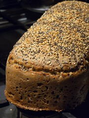 A close-up shot of a freshly baked loaf of brown bread with a crisp crust and a generous topping of various poppy and sesame seeds.