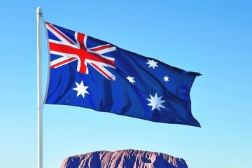 Australian flag waving proudly against a clear blue sky with red rock formations in the foreground