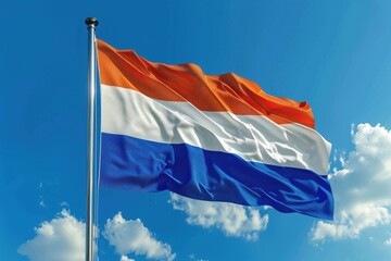 National flag of the Netherlands waving against a clear blue sky with clouds during a sunny day