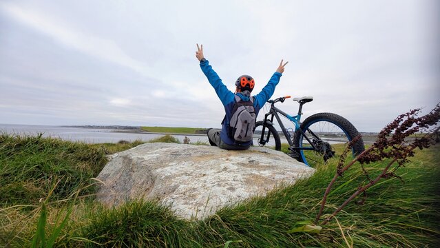 Adventure cyclist with mountain bike celebrating success on Wild Atlantic Way near Silverstrand Beach Galway, scenic Ireland coastline, freedom outdoor travel fitness lifestyle, exploration