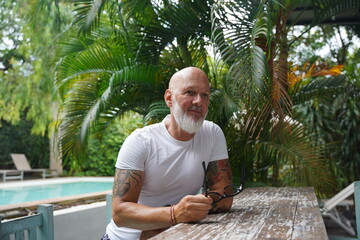 A man with a beard poses near a table in a park.