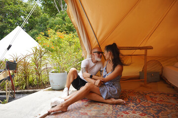 A man and a woman are comfortably sitting together inside of a tent