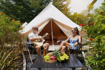 A man plays guitar for a woman near a cozy tent at a glamping site.