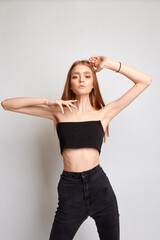 Fototapeta premium A beautiful woman with a perfect figure is wearing black trousers and a black top. She stands on a white background in the studio.