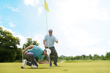 Asian golfer putting on green with senior cheering nearby.