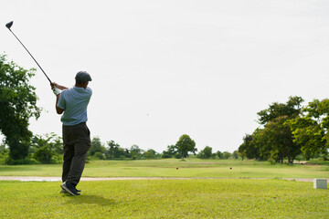 Obraz premium Senior Asian golfer teeing off under morning sunlight.