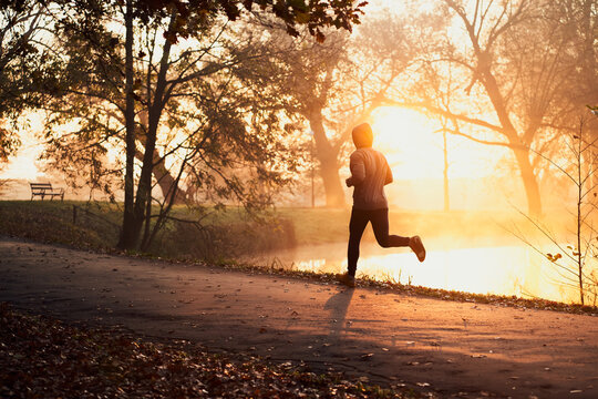 Active man jogging in park during autumn sunny morning