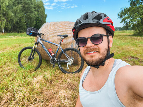Happy cyclist takes a selfie in a sunny field with his mountain bike
