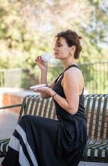 Woman in black dress sitting on bench with coffee cup outdoors