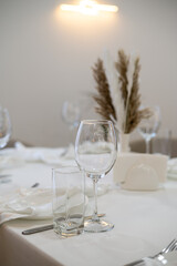 Stylish restaurant interior featuring a neatly set white table with glassware and dried flowers. Soft warm lighting and minimalist decor create an elegant dining atmosphere.