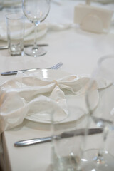 Detail of an elegant restaurant table with folded white napkin, wine glass, and cutlery. Minimalist design and soft lighting create a refined, luxurious dining atmosphere.