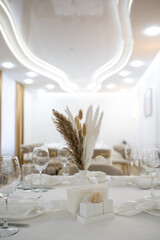 Elegant restaurant hall with neatly arranged white table, glassware, and dried flower centerpiece. Bright lighting and modern design create a refined, cozy atmosphere.