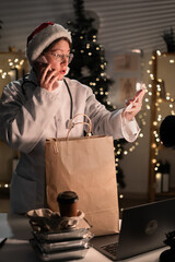 Young female doctor in eyeglasses and Santa Claus hat on the shift unpacking takeaway food in paper bag working at night on Christmas Eve in hospital. Holidays, medicine and consumption