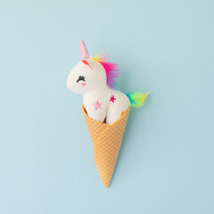 Toy unicorn inside waffle cone on blue background. Creative pop art composition with humor and imagination.