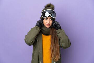 Skier caucasian girl with snowboarding glasses isolated on purple background frustrated and covering ears