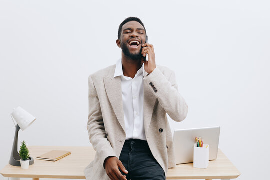 Fototapeta Confident young smiling man talking on mobile phone in modern office, casual business attire, cheerful expression, light background, workspace with laptop and greenery, professional lifestyle concept